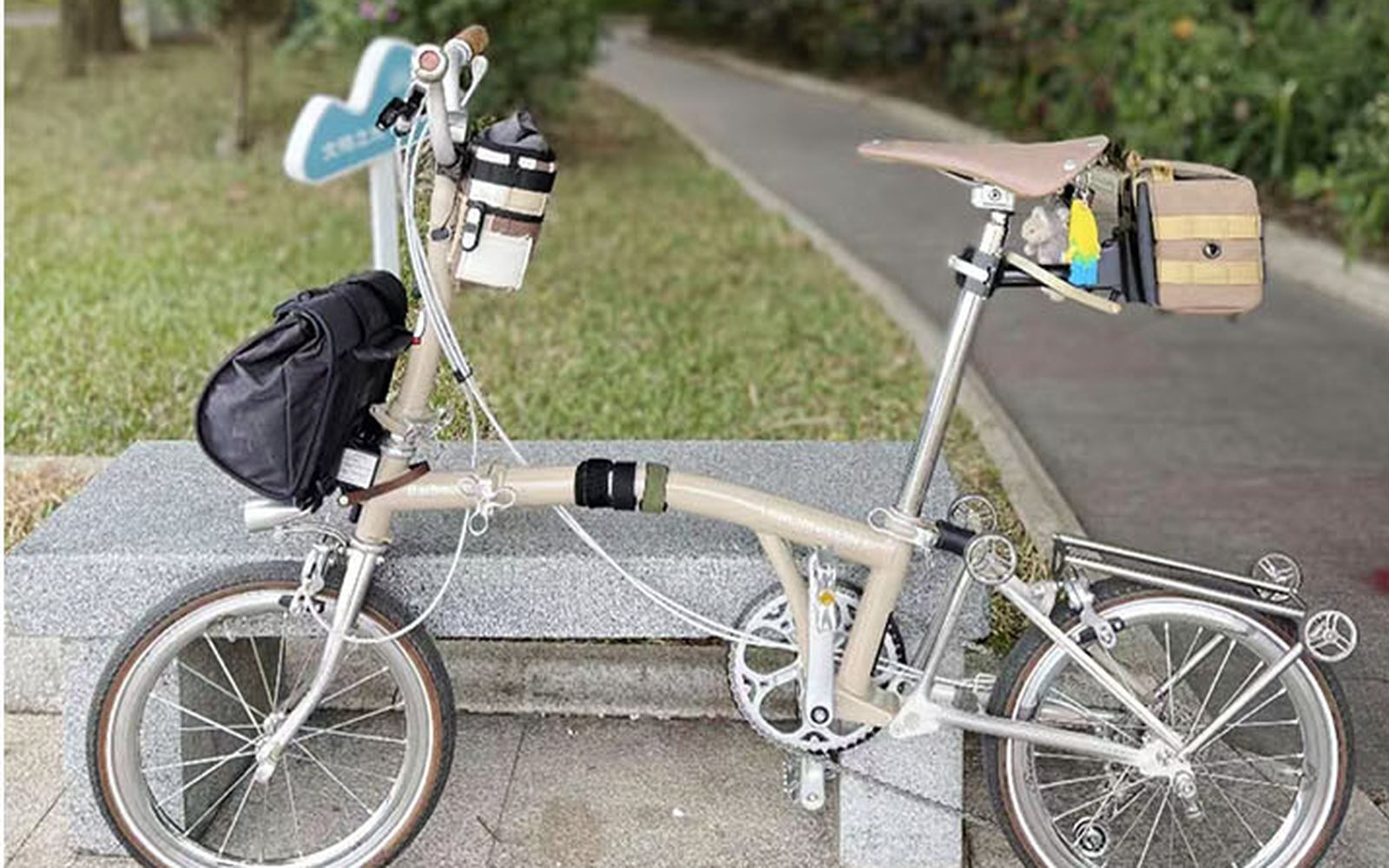 Beige Brompton with a small tan saddlebag in a park