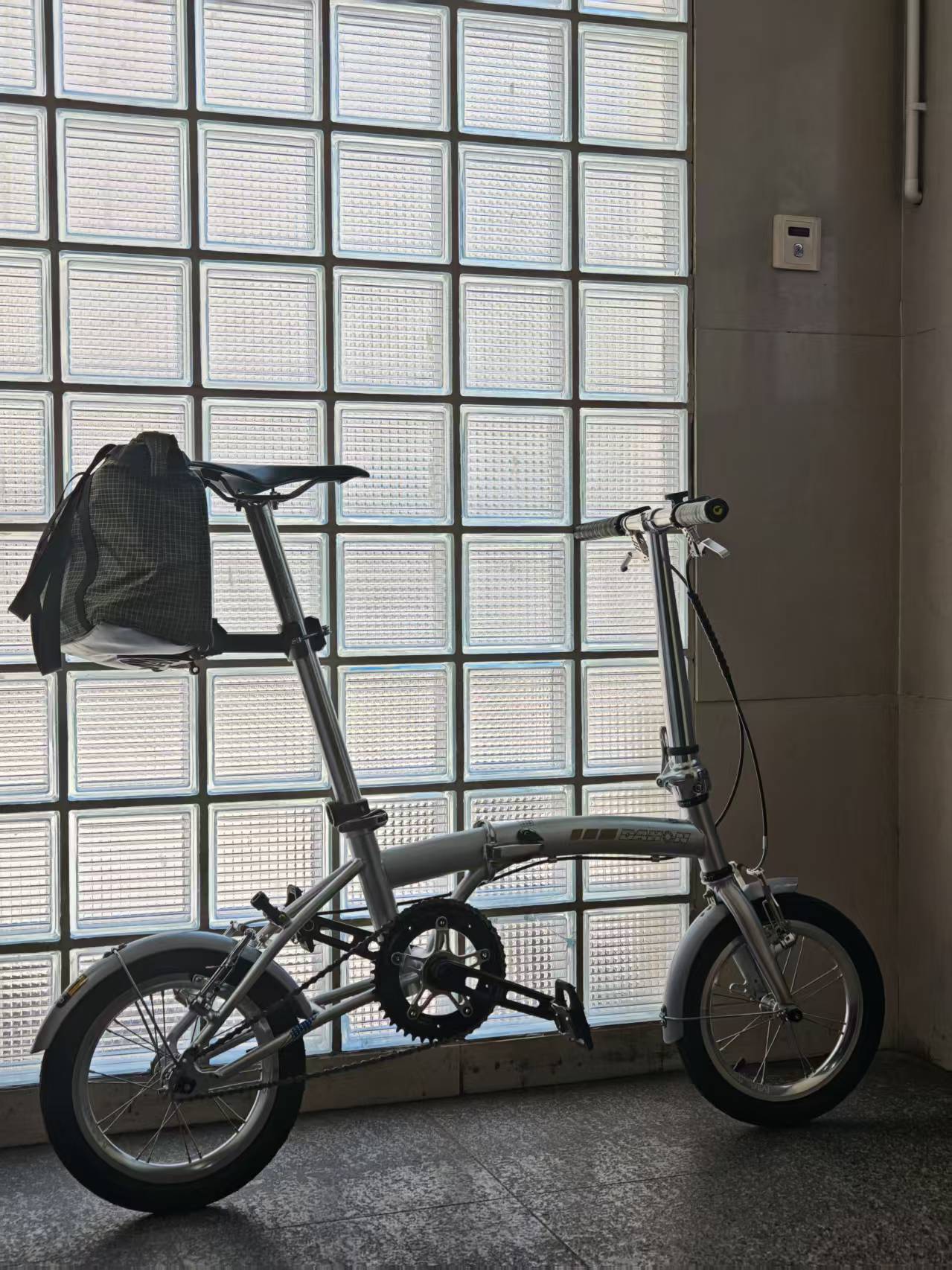 Silver folding bike with a checkered backpack mounted behind the saddle